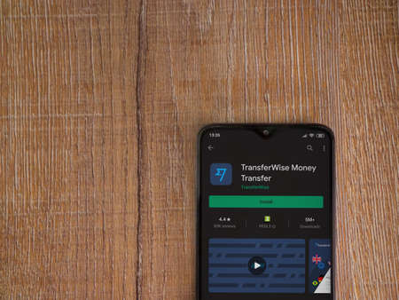 Lod, Israel - July 8, 2020: TransferWise app play store page on the display of a black mobile smartphone on wooden background. Top view flat lay with copy space.のeditorial素材