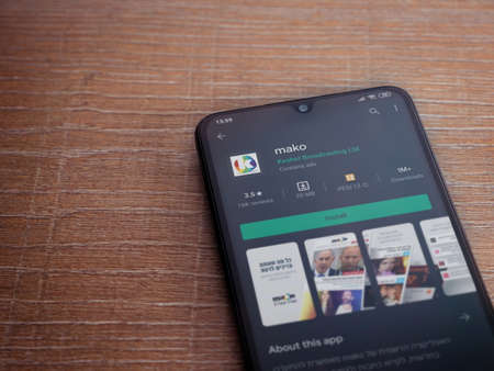 Lod, Israel - July 8, 2020: mako app play store page on the display of a black mobile smartphone on wooden background. Top view flat lay with copy space.のeditorial素材