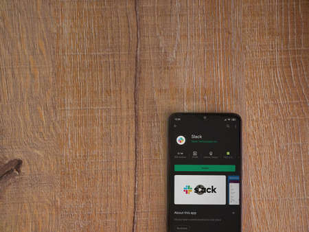 Lod, Israel - July 8, 2020: Slack app play store page on the display of a black mobile smartphone on wooden background. Top view flat lay with copy space.のeditorial素材
