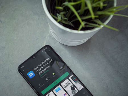 Lod, Israel - July 8, 2020: Modern minimalist office workspace with black mobile smartphone with Maxthon Browser app play store page on marble background. Top view flat lay with copy space.のeditorial素材