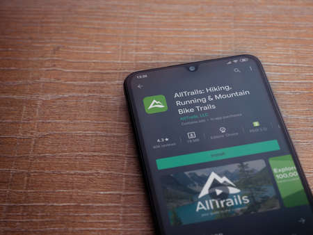 Lod, Israel - July 8, 2020: AllTrails app play store page on the display of a black mobile smartphone on wooden background. Top view flat lay with copy space.のeditorial素材
