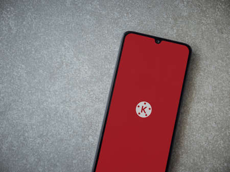 Lod, Israel - July 8, 2020: KineMaster - Video Editor and Movie Maker app launch screen with logo on the display of a black mobile smartphone on ceramic stone background. Top view flat lay with copy space.のeditorial素材