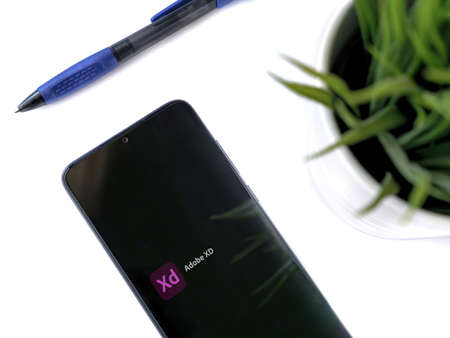 Lod, Israel - July 8, 2020: Modern minimalist office workspace with black mobile smartphone with Adobe XD app launch screen with logo on a white background. Close up top view flat lay.のeditorial素材