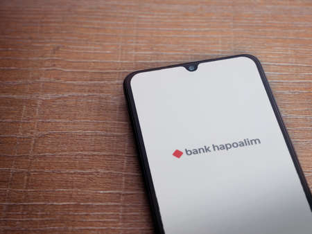 Lod, Israel - July 8, 2020: Bank Hapoalim app launch screen with logo on the display of a black mobile smartphone on wooden background. Top view flat lay with copy space.のeditorial素材