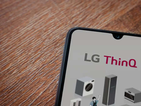 Lod, Israel - July 8, 2020: LG ThinQ app launch screen with logo on the display of a black mobile smartphone on wooden background. Top view flat lay with copy space.のeditorial素材