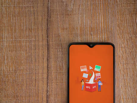 Lod, Israel - July 8, 2020: WPS Office app launch screen with logo on the display of a black mobile smartphone on wooden background. Top view flat lay with copy space.のeditorial素材