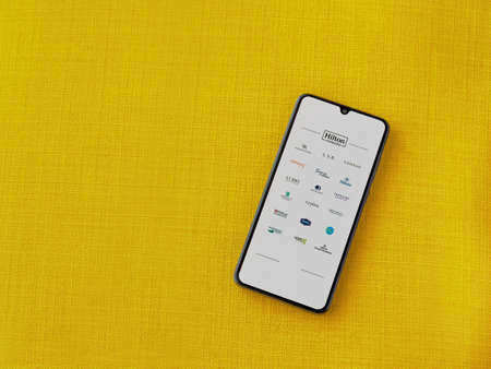 Lod, Israel - July 8, 2020: Hilton Honors app launch screen with logo on the display of a black mobile smartphone on a yellow fabric background. Top view flat lay with copy space.のeditorial素材