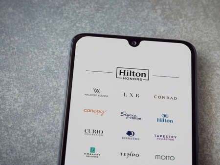 Lod, Israel - July 8, 2020: Hilton Honors app launch screen with logo on the display of a black mobile smartphone on ceramic stone background. Top view flat lay with copy space.のeditorial素材