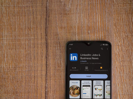 Foto de Lod, Israel - July 16,2023: LinkedIn app play store page on smartphone on wooden background. Top view flat lay with copy space. - Imagen libre de derechos