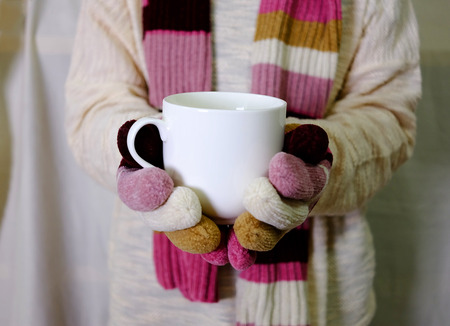 Hand holding warm milk with white sweater, scarf and cozy hand glovesの写真素材