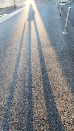Black long morning shadow of people on the streetside