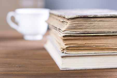 Stack of old books on wooden table and coffee in backgroundの写真素材