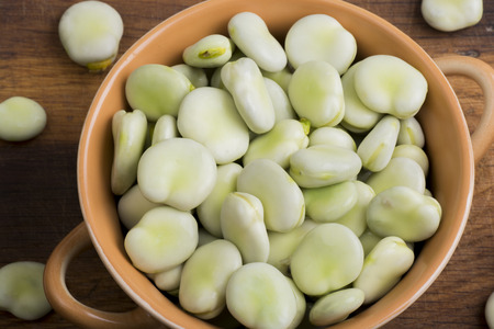 Fresh broad beans in bowl on wooden board