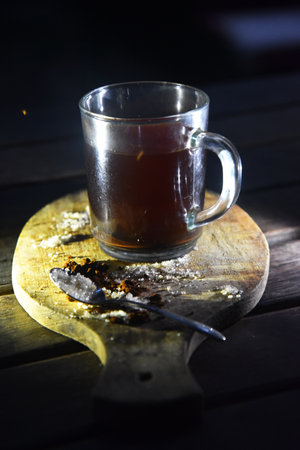 A cup of coffee on the wooden table, with sugar and coffee powder arround themの写真素材