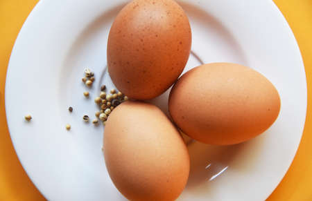 Chicken eggs placed on white plate with some white pepper on color background