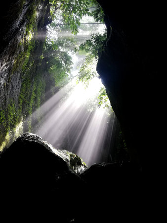 The sun shines through the dark cave in the jungle of Thailand.の写真素材