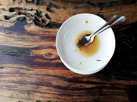 Dirty plate with spoon and fork on wooden table in coffee shop