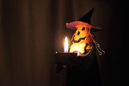 A Halloween decoration that has the face of a Jack-o-Lantern and the pointy hat of a witch. Shot in the dark using only the candle as the light source.の写真素材