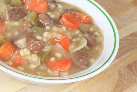 Beef and Barley Stew in a bowl sitting on a wooden table.の写真素材
