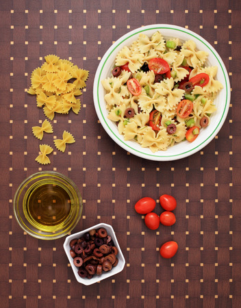 A bowl of pasta salad and the ingredients to make itの写真素材