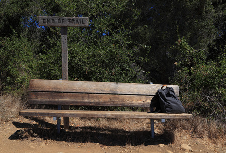 At the end of the hiking trail, a backpack sits at the end of an empty wooden bench.の写真素材