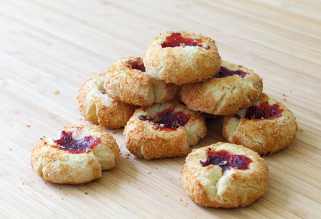 A batch of coconut cookies with raspberry jam filling on a wooden table.の写真素材