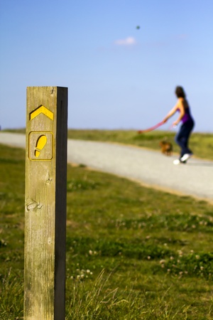Image of a footpath sign with woman throwing a ball for her dog in the backgroundの写真素材