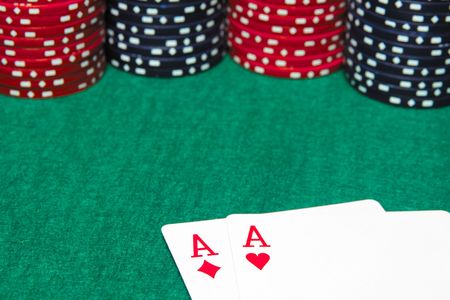 Focusing on a pair of aces and poker chips on a green table.