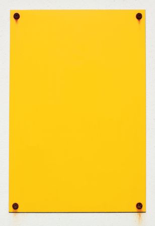 Blank yellow sign stuck to a white wall with rusty screws.の写真素材