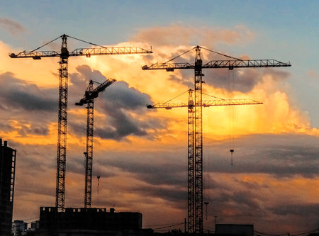 Construction cranes on the background of the sunset sky. Bright clouds and silhouettes of tower cranes.の写真素材