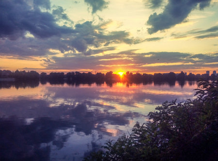 Sunset on the lake. Smooth water surface, clouds and sun. Calm summer evening.の写真素材