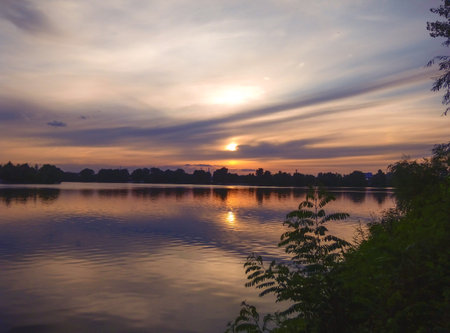 Sunset on the lake. Smooth water surface, clouds and sun. Calm summer evening.の写真素材