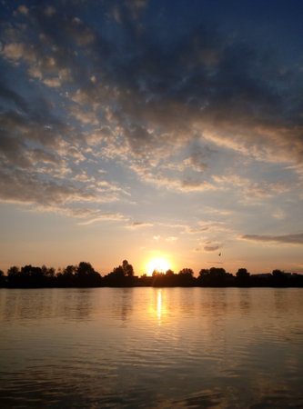 Sunset on the lake. Smooth water surface, clouds and sun. Calm summer evening.の写真素材