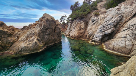 Seascape with calm water surface and rocks. Turquoise transparent water. Evening on the Mediterranean coast.の写真素材