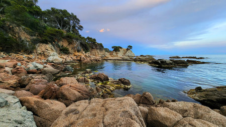 Evening seascape with calm water surface and cliffs. Turquoise water and big stones on the...