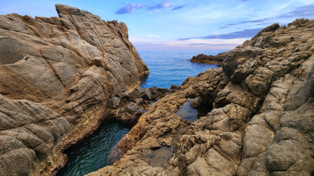 Evening seascape with calm water surface and cliffs. Turquoise water and big stones on the...