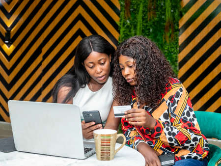 two female friends making payment online holding credit card using laptop technology with mobile mobileの写真素材