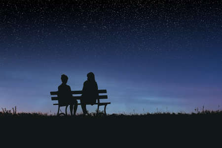 Silhouettes of two female friends sitting together, talking and watching a spectacular night skyの写真素材