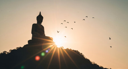 Buddha statue on the mountain at sunset with flying birds.の素材