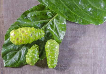 Fruit of Great morinda (Noni) or Morinda citrifolia tree and green leaf on the wood backgroundの写真素材