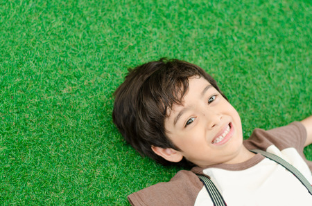 Little boy lay down on green grassの写真素材