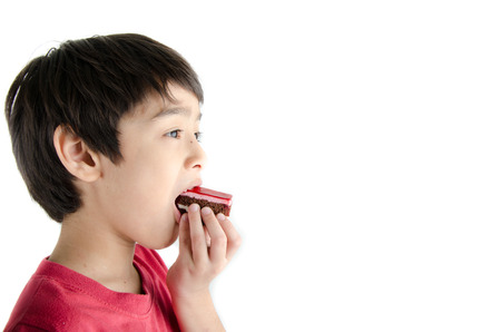 Little asian boy eating long cherry cake on white background
