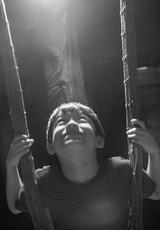 Little boy playing swing indoor rim light black and whiteの写真素材