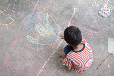Little boy drawing and coloring by chalk on the groundの写真素材