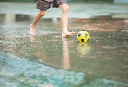 Little boy kicking ball in the water logging on the streetの写真素材