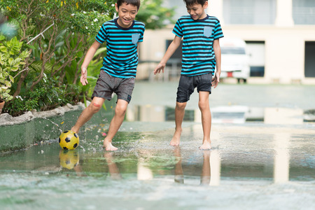 Little boy kicking ball in the water logging on the streetの写真素材
