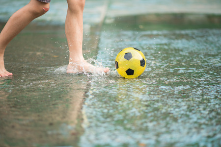 Little boy kicking ball in the water logging on the streetの写真素材
