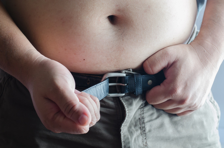 Close up of man's belly trying wear his belt with tightの写真素材