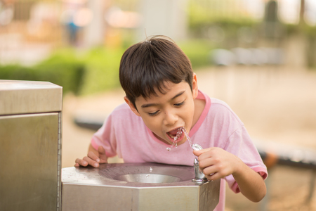 Little asian boy drinking water in the public park の写真素材