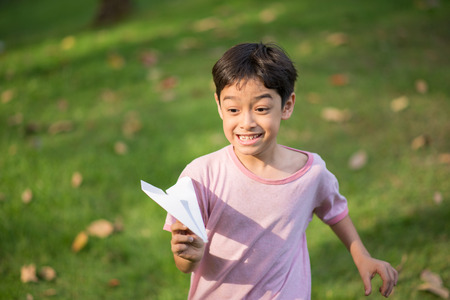 Little asian boy playing plane paper in the park の写真素材